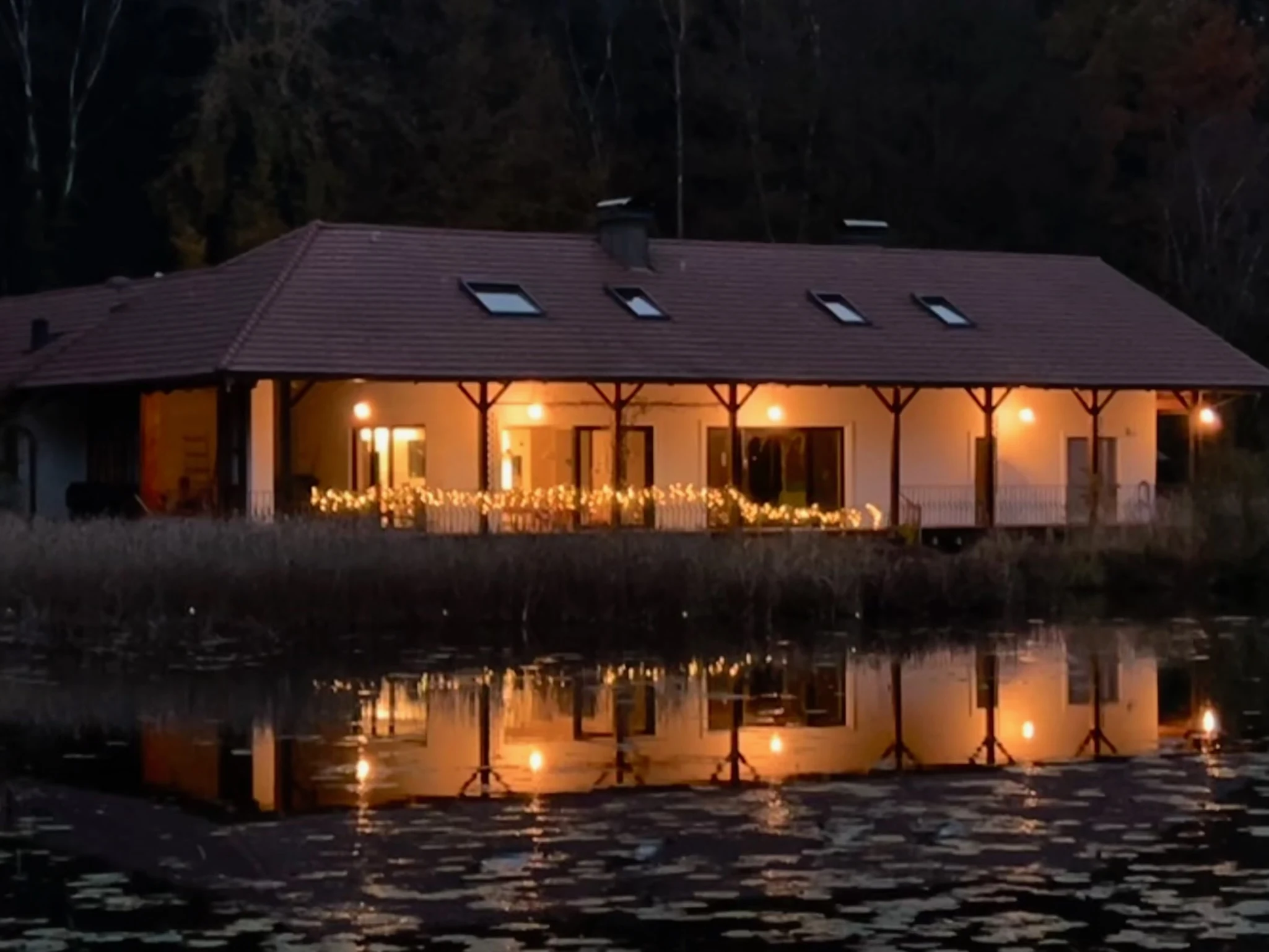 Warm beleuchtetes Haus am Abend mit Spiegelung im Teich